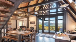 Un comedor amplio con una gran mesa de madera dispuesta para seis comensales, una cocina moderna con estufa y vistas panorámicas a través de amplios ventanales.