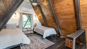 Dormitorio tipo loft con techo inclinado, dos camas, un tapete estampado y un banco de madera.