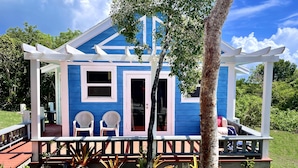 Una casa azul con porche, dos sillas blancas y un pequeño jardín.