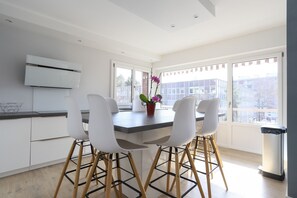 A modern kitchen with white cabinets, a central island with chairs, and large windows offering a view of the city.