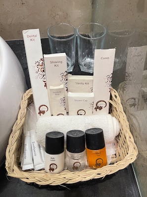 A bathroom with a wicker basket containing toiletries, including a dental kit, shaving kit, vanity kit, sanitary bag, and shower cap. - Grand Mongolia Hotel (Rawalpindi)