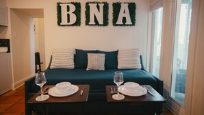 A neatly arranged room with a bed, two side tables with dinnerware, and a wall decoration spelling "BNA".