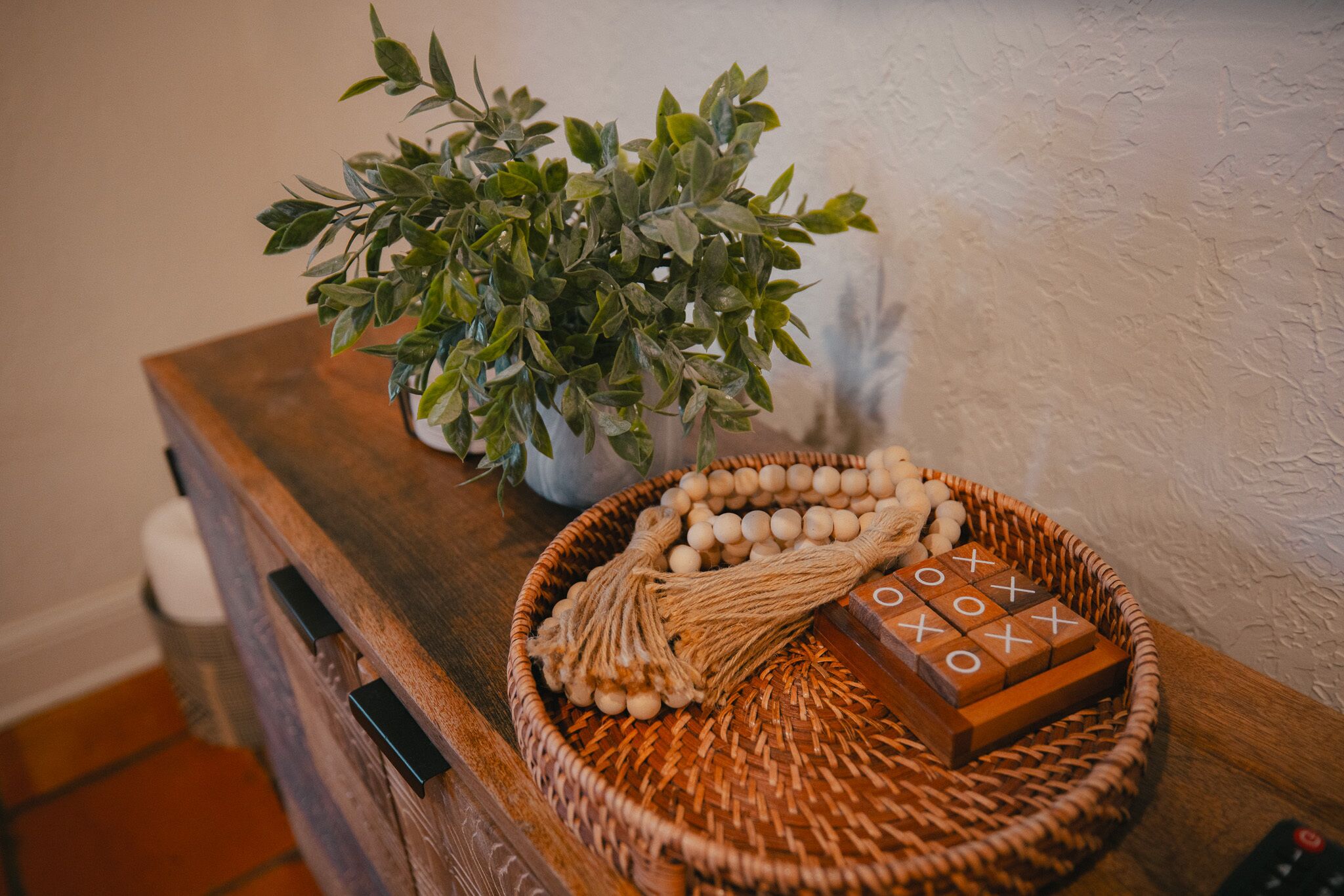 A wooden table with a woven basket containing wooden blocks and a string of beads, a potted plant, and a remote control.