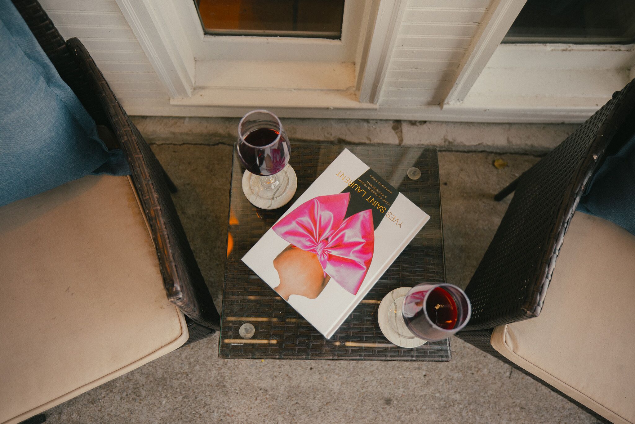 Una mesa con un libro, dos copas de vino tinto y sillas de mimbre.