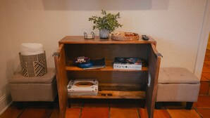 A wooden console table with a potted plant, a basket, and a remote control. There are two cushioned stools on either side.