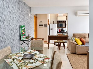 A modern living room with a glass dining table, a sofa, and a kitchen area in the background. - Nautilus Paradise in Penha-SC (Penha)