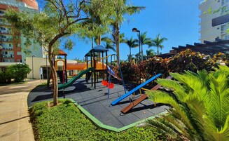 Un parque infantil con toboganes y estructuras para escalar, rodeado de vegetación y edificios.