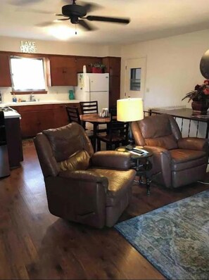 A living room with two leather chairs, a dining table, and a kitchen in the background.