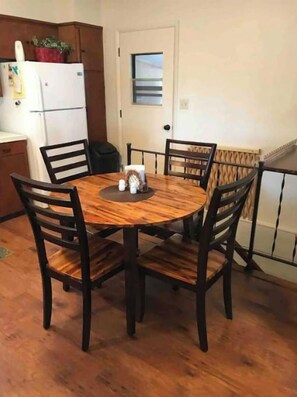 A dining area with a round wooden table and four chairs, a white refrigerator, and a door with a window.