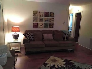 A living room with a sofa, a lamp, and a wall with various framed pictures.