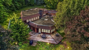 Een modern huis met een gebogen dak, een terras en een groot raam dat uitkijkt op een weelderige tuin.
