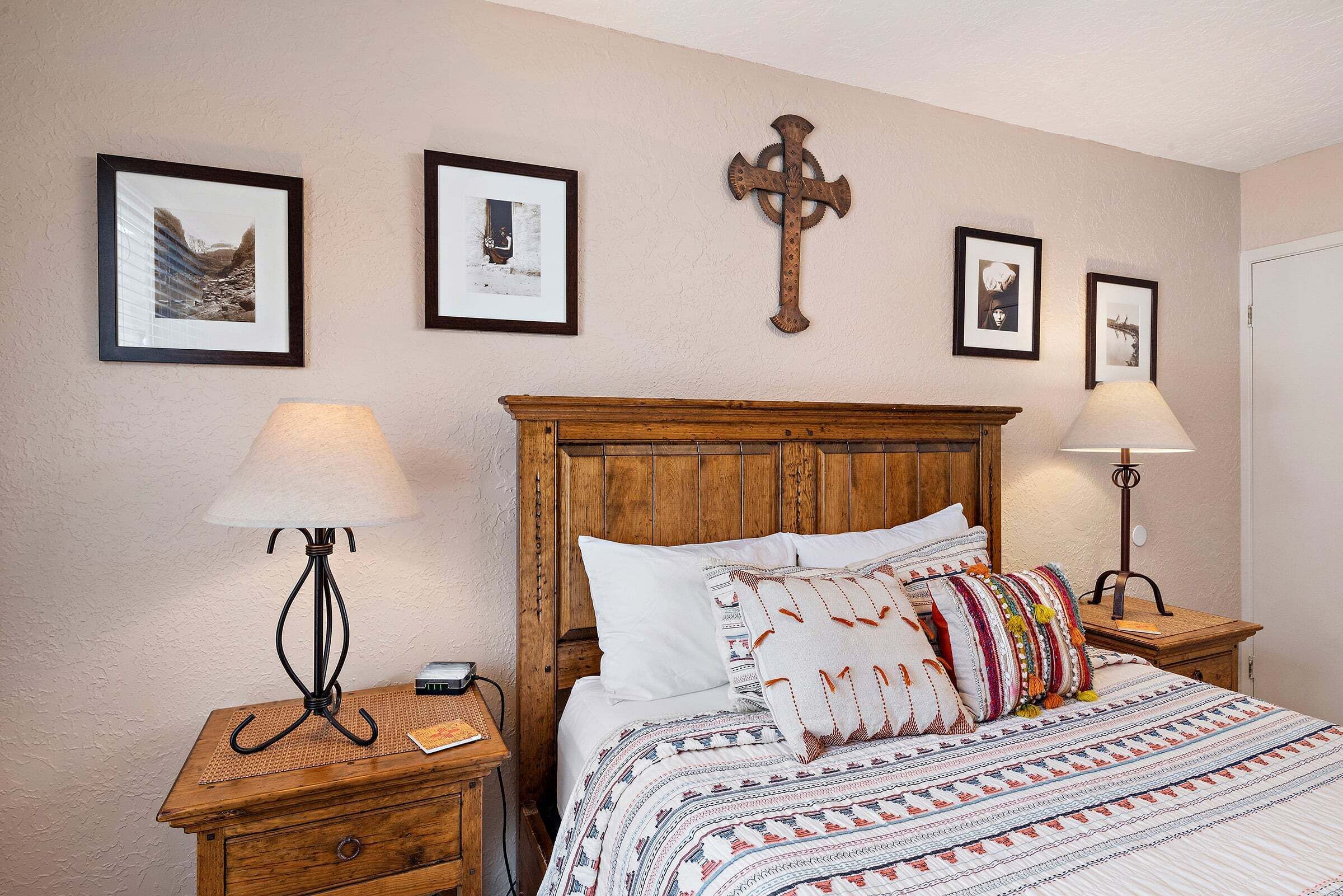 Een slaapkamer met een houten hoofdeinde, een bed met een decoratieve spreideken en ingekaderde foto's aan de muur.
