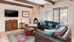 A living room with a fireplace, a leather sofa, a coffee table, and a TV mounted on the wall. - Fort Marcy 35 | Just Like Home - But Even Better! 2-Bdrm, Walk To Plaza, Fireplace (Santa Fe)