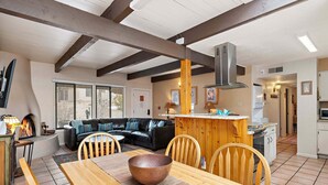 A spacious living area with a wooden dining table, a black leather sofa, and a kitchen in the background. - Fort Marcy 35 | Just Like Home - But Even Better! 2-Bdrm, Walk To Plaza, Fireplace (Santa Fe)