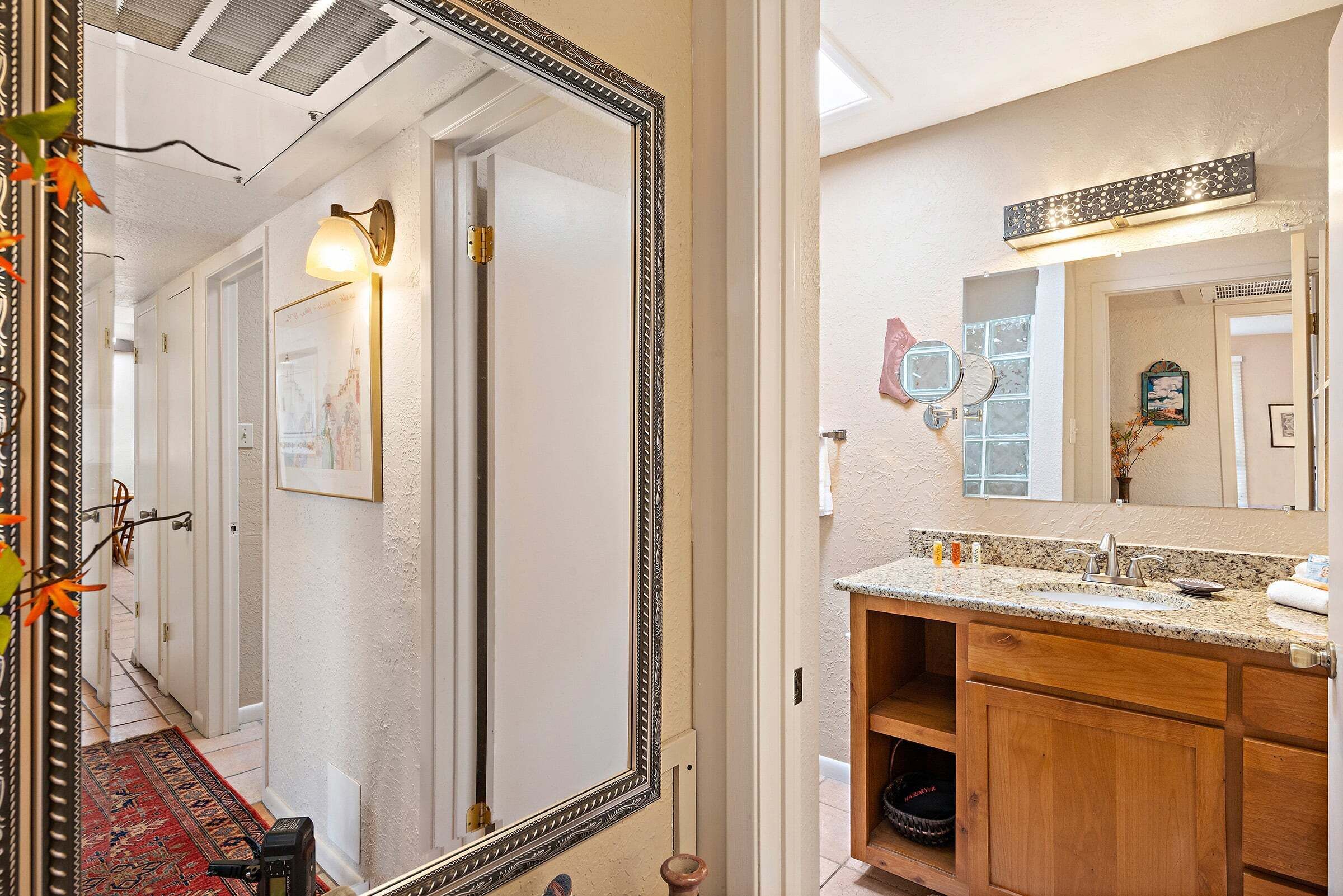 A bathroom with a granite countertop, wooden cabinets, a large mirror, and a wall-mounted light fixture.