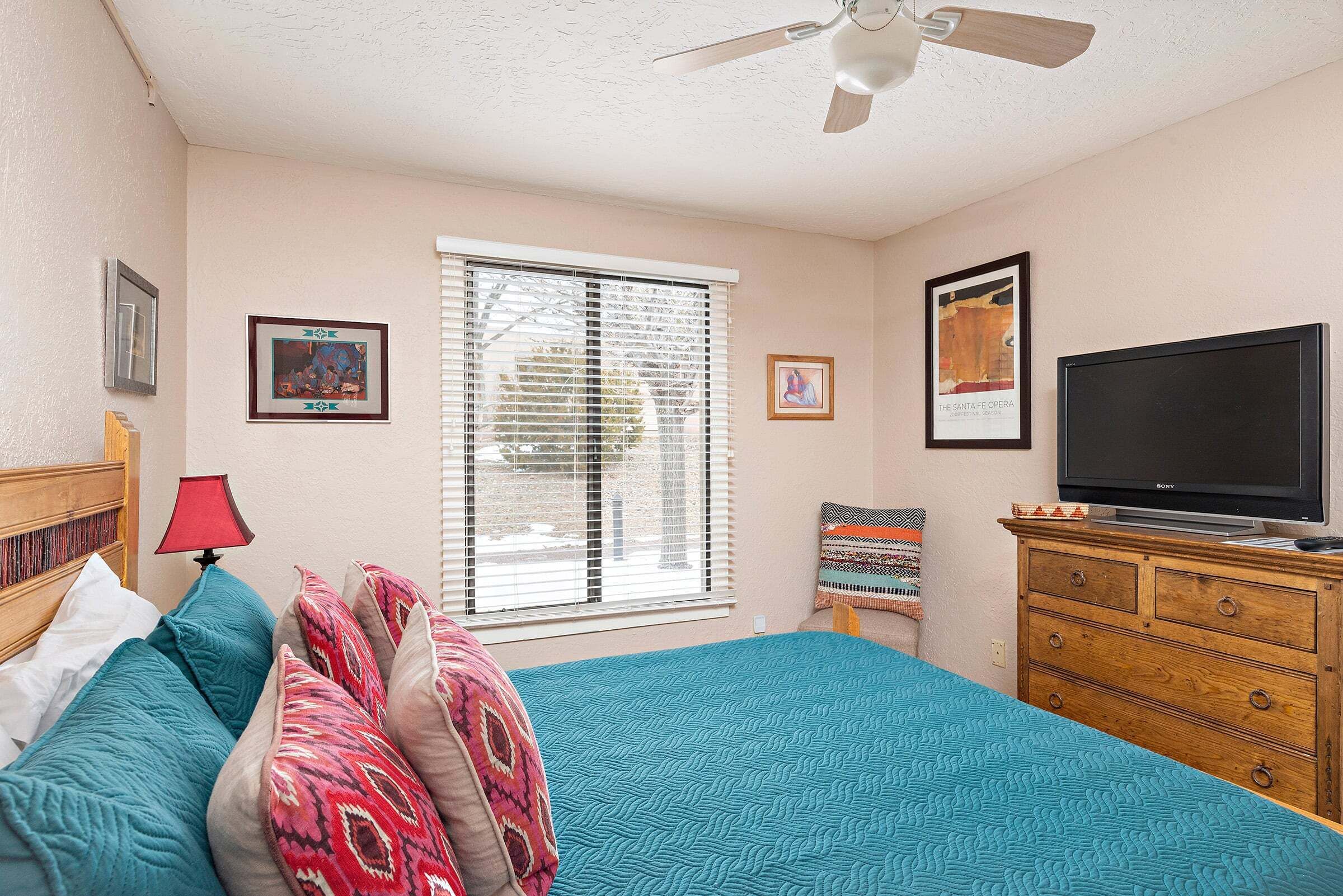 A bedroom with a bed, a dresser, a television, and a window with blinds.