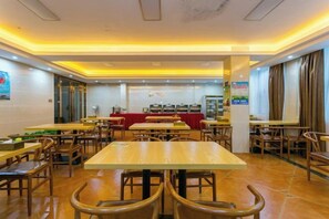 Un restaurant avec plusieurs tables et chaises, un comptoir où sont exposés des plats, et une nappe rouge.
