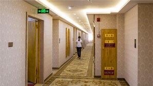 A hotel hallway with patterned carpet, wooden doors, and signs indicating fire safety equipment.