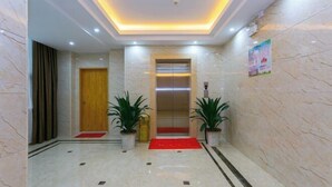 A lobby with a marble floor, a wooden door, an elevator, and potted plants.