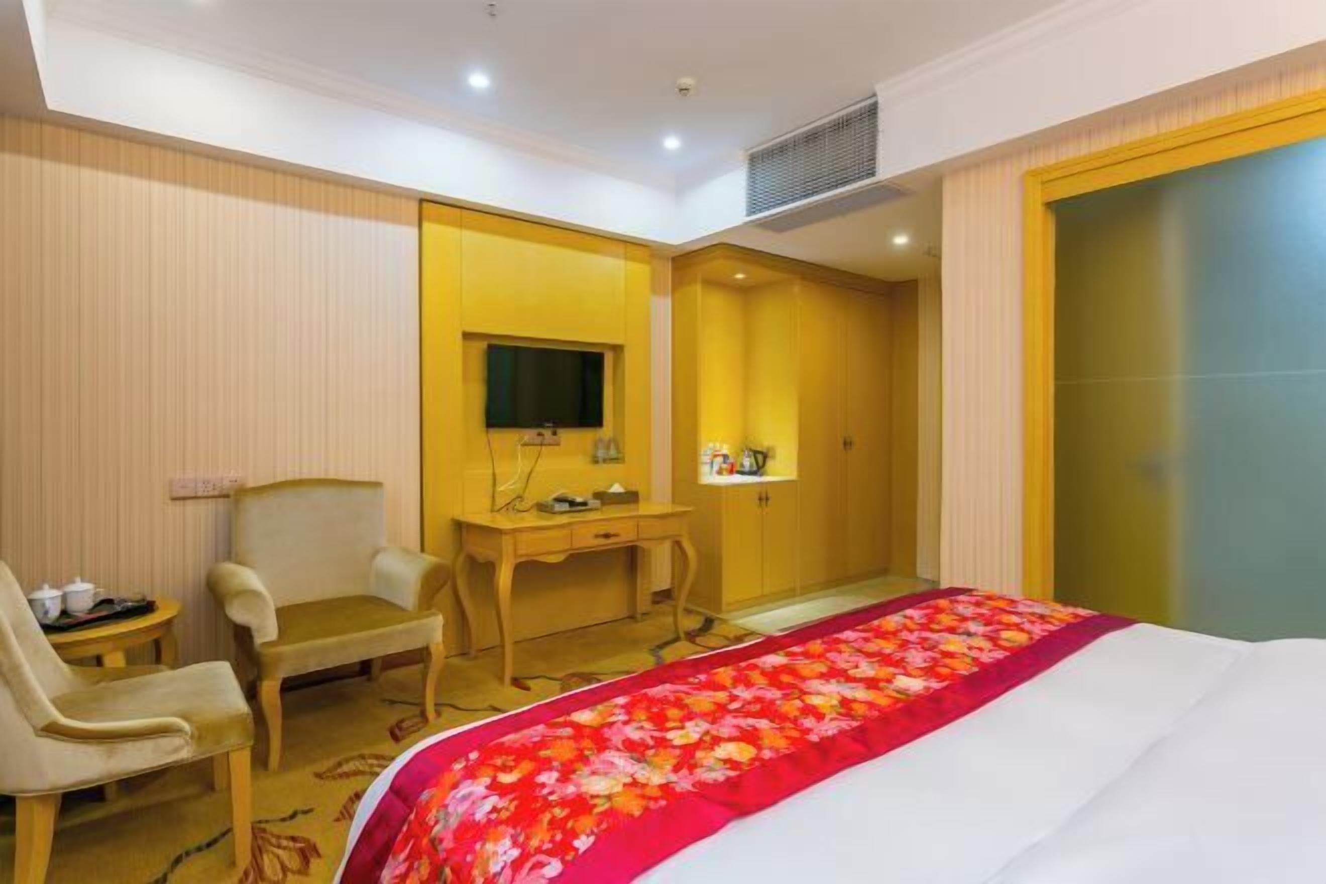 A hotel room with a bed, a desk, a chair, a television, and a wardrobe.