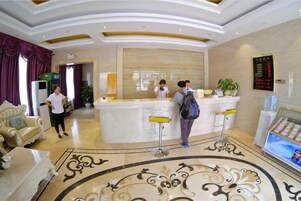 A hotel lobby with a reception desk, a seating area with a sofa, and a decorative floor pattern.