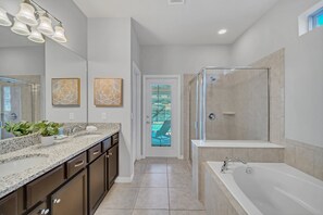 A modern bathroom with a large mirror, a walk-in shower, a bathtub, and a granite countertop with a sink.