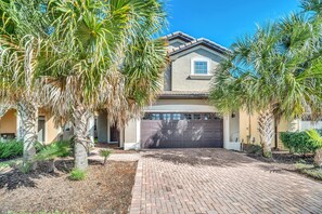 A residential house with a brick driveway, palm trees, and a garage.