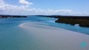 A coastal landscape with a sandy beach, clear turquoise waters, and a distant shoreline with vegetation. - Castaway at Pelican – Relaxed, Pet Friendly Stay Near Lake And Beach (Pelican)