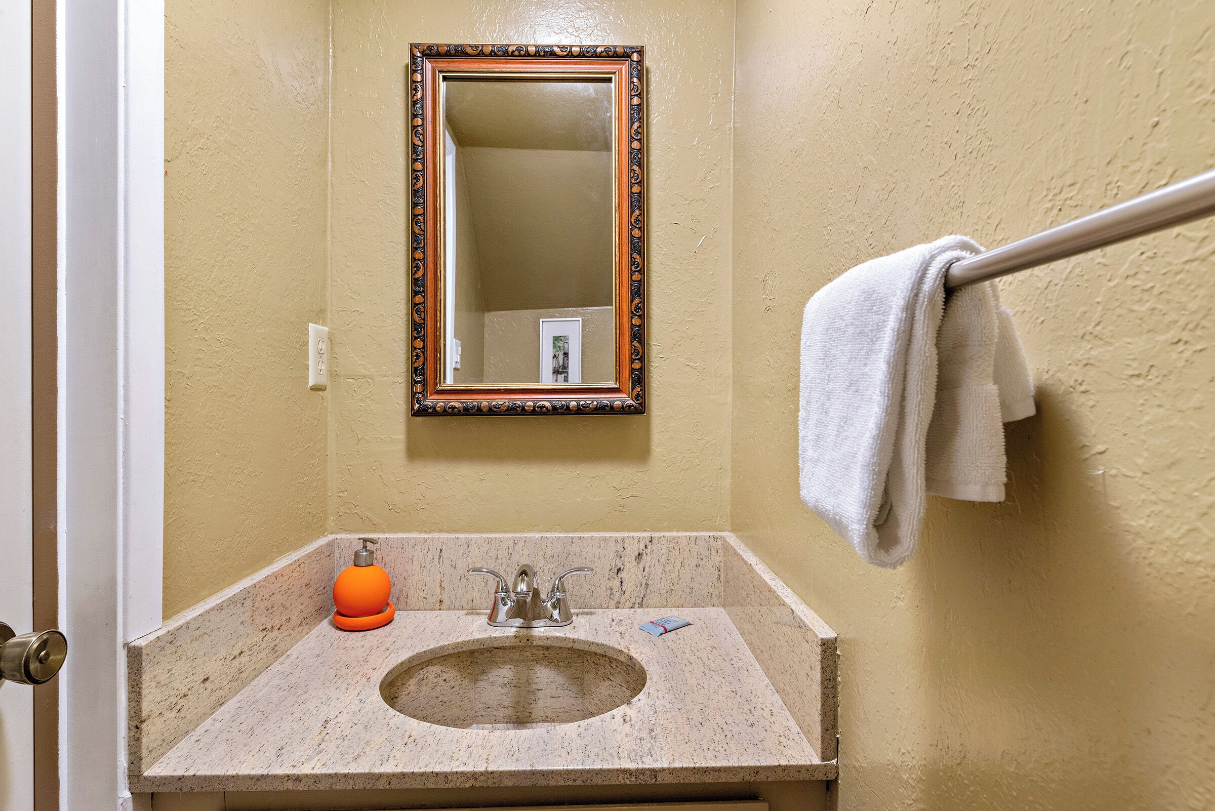 Un baño con lavabo, espejo, toallero y dispensador de jabón naranja.