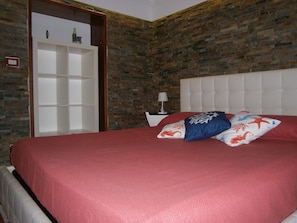 Quarto com parede de tijolos, cabeceira branca e colcha vermelha.