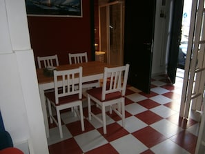 Uma sala de jantar com chão xadrez vermelho e branco, cadeiras brancas e uma mesa de madeira.