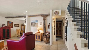 A spacious living area with a red sofa, wooden furniture, and a staircase with black railings. - Fort Marcy 43 | Walk to Plaza | Kiva Fireplace | Full Kitchen | Hot Tub | Pool | 2 Levels (Santa Fe)