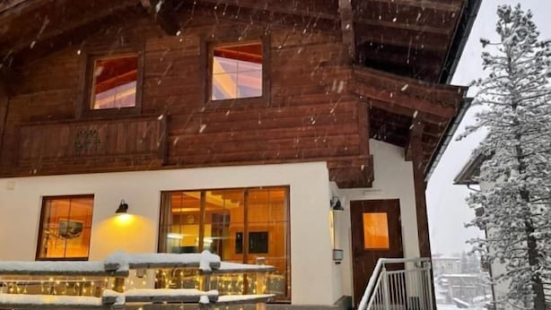 Un chalet en bois doté d’un balcon et de grandes fenêtres, entouré de neige.
