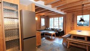 Un intérieur de chalet chaleureux avec un sol en pierre, des poutres en bois, un réfrigérateur, un canapé et un coin repas.