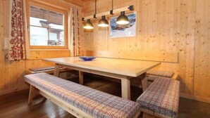 Un intérieur en bois avec une grande table et des bancs, des luminaires suspendus et une fenêtre avec des rideaux.