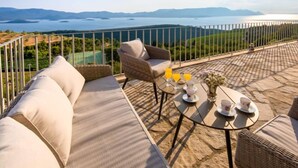 Une terrasse avec un canapé, une chaise, une table avec des tasses et des verres, et une vue sur un lac et des montagnes.