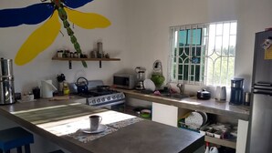 A kitchen with a gas stove, microwave, kettle, and various utensils. There is a window with bars and a shelf above the sink. - Dragonfly - House- Short walk to beach (Treasure Beach)
