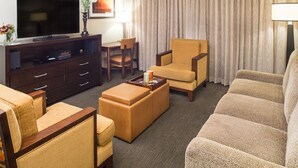 Ein Hotelzimmer mit einer Sofagarnitur, einem Fernseher, einem Couchtisch und einem Schreibtisch mit Stuhl.