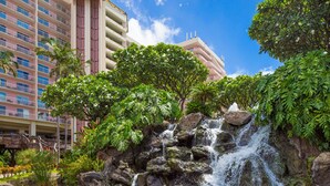 Ein Hotel mit einem Wasserfall, üppiger Vegetation und einem mehrstöckigen Gebäude im Hintergrund.