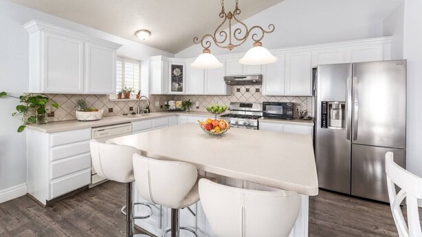 A modern kitchen with white cabinetry, stainless steel appliances, and a central island with bar stools.