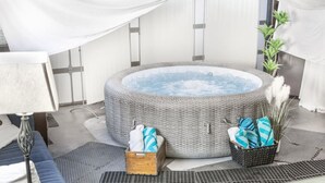 A modern spa room with a hot tub, a wooden side table, and a floor mat.