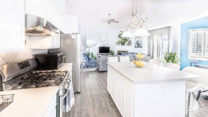 A modern kitchen with a central island, a dining area with a white table, and a living room with a sofa and TV.