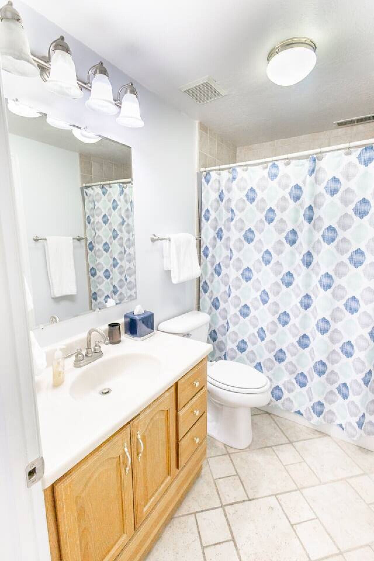 A bathroom with a white sink, wooden cabinets, a toilet, and a shower curtain with a blue and white pattern.