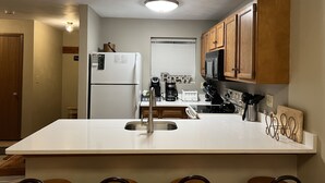 Una cucina con un piano di lavoro bianco, mobili in legno, un frigorifero, un forno a microonde e una macchina per il caffè.