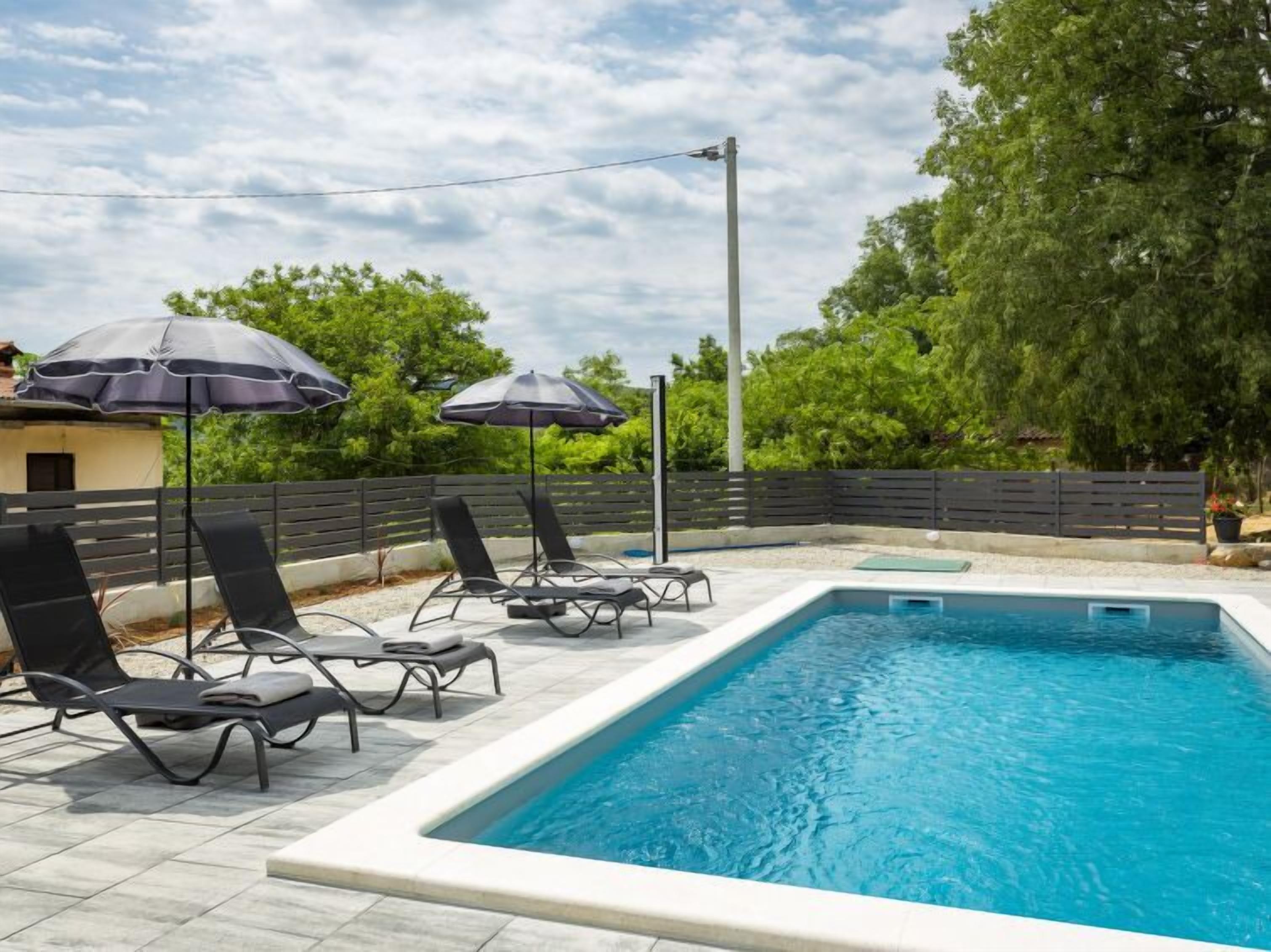 Piscina rectangular con solárium empedrado, rodeada de sillones de baño negros y sombrillas.