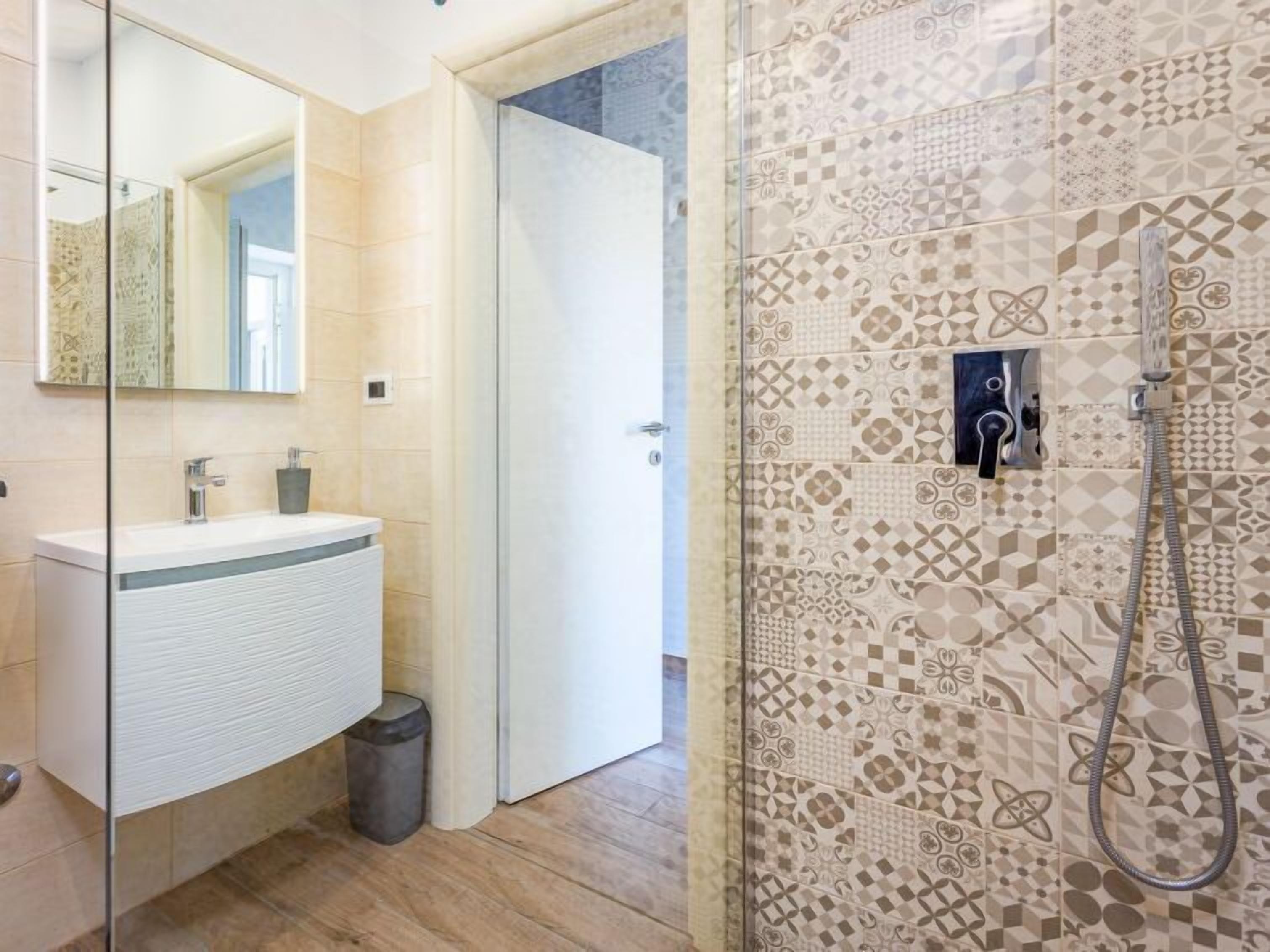 A modern bathroom with a glass shower enclosure, a white sink, and patterned tiles.