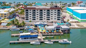 Marina con barcos amarrados, un gran edificio de hotel y un área de bar frente al agua.