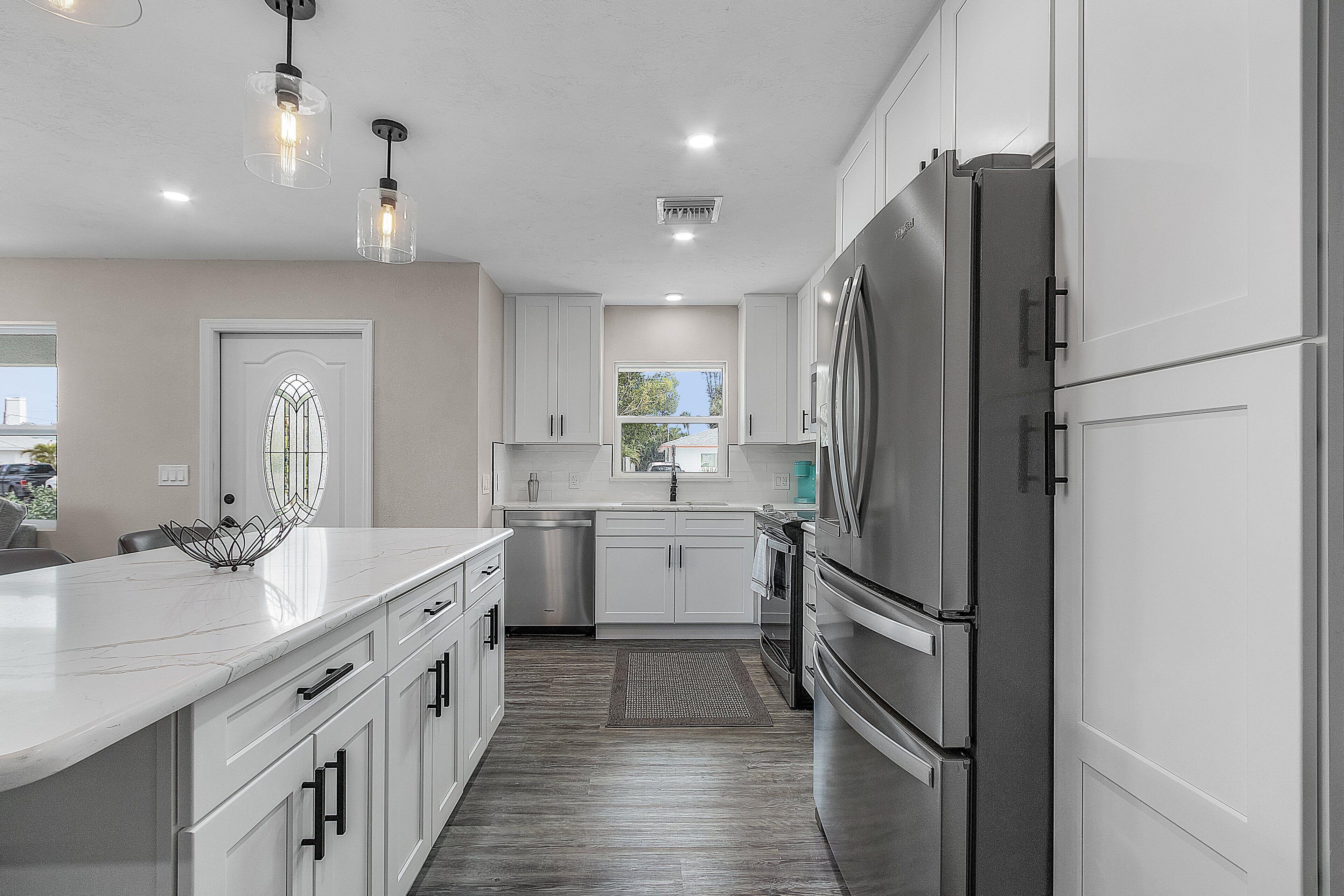 A modern kitchen with white cabinetry, stainless steel appliances, and pendant lighting.