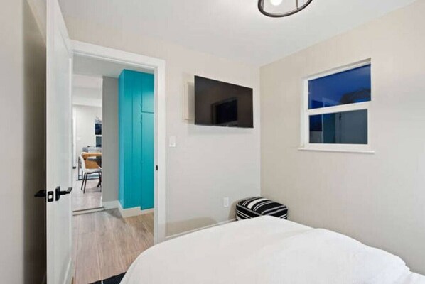 A bedroom with a bed, a television mounted on the wall, a window, and a door leading to another room.