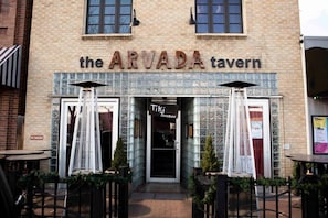 The ARVADA tavern with a tiled facade, two large windows, and outdoor seating with umbrellas.